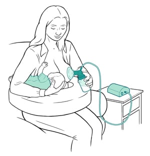 Female sitting to breastfeed baby on one breast and pump milk on the other breast. 